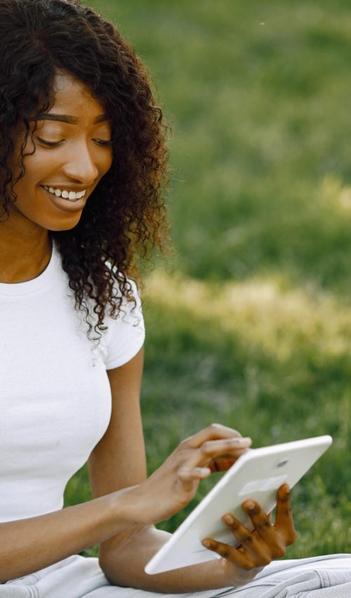 female-african-student-sitting-on-a-grass-and-usin-2022-06-09-15-30-38-utc-min